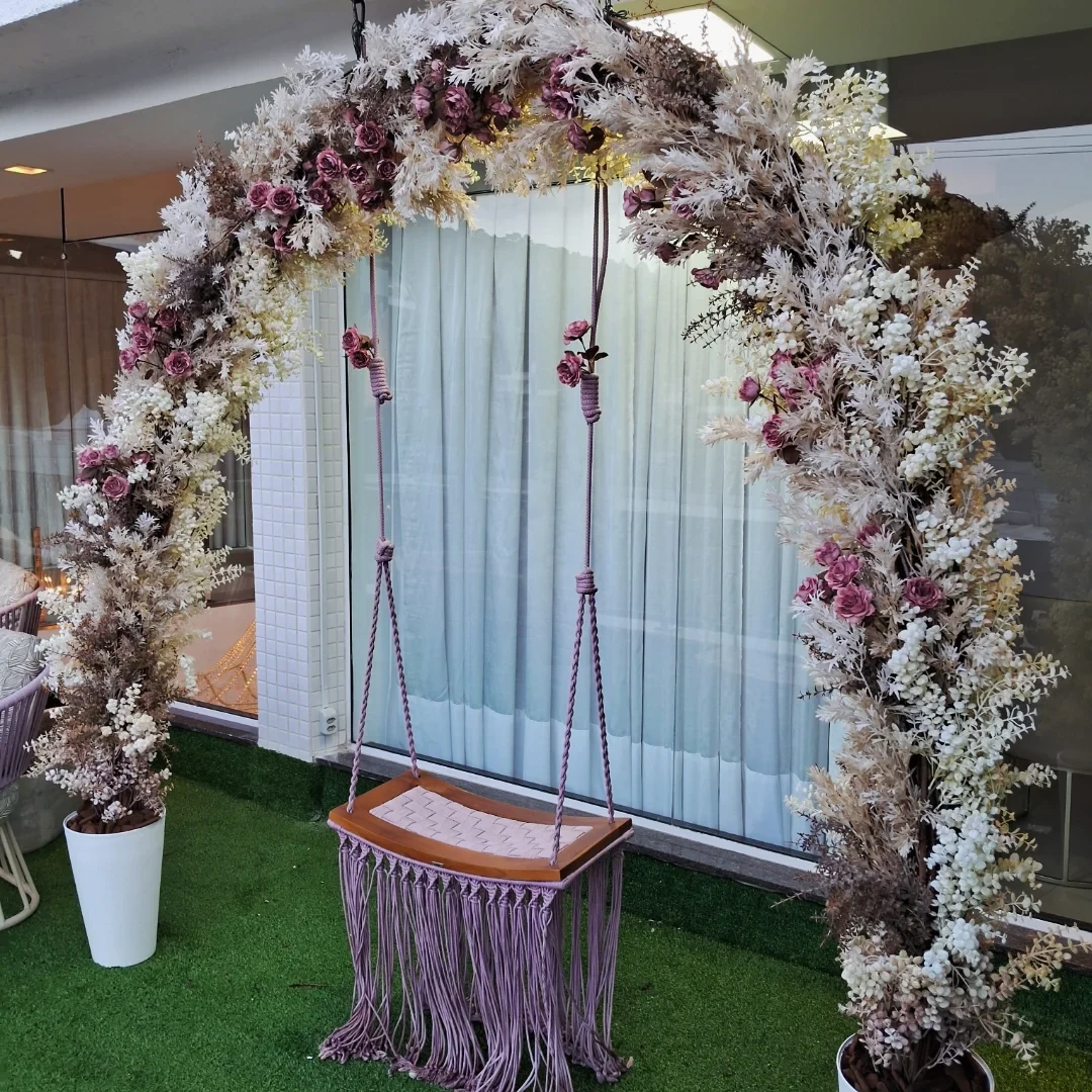 Arco de flores permanentes envolvendo balanço artesanal em área externa